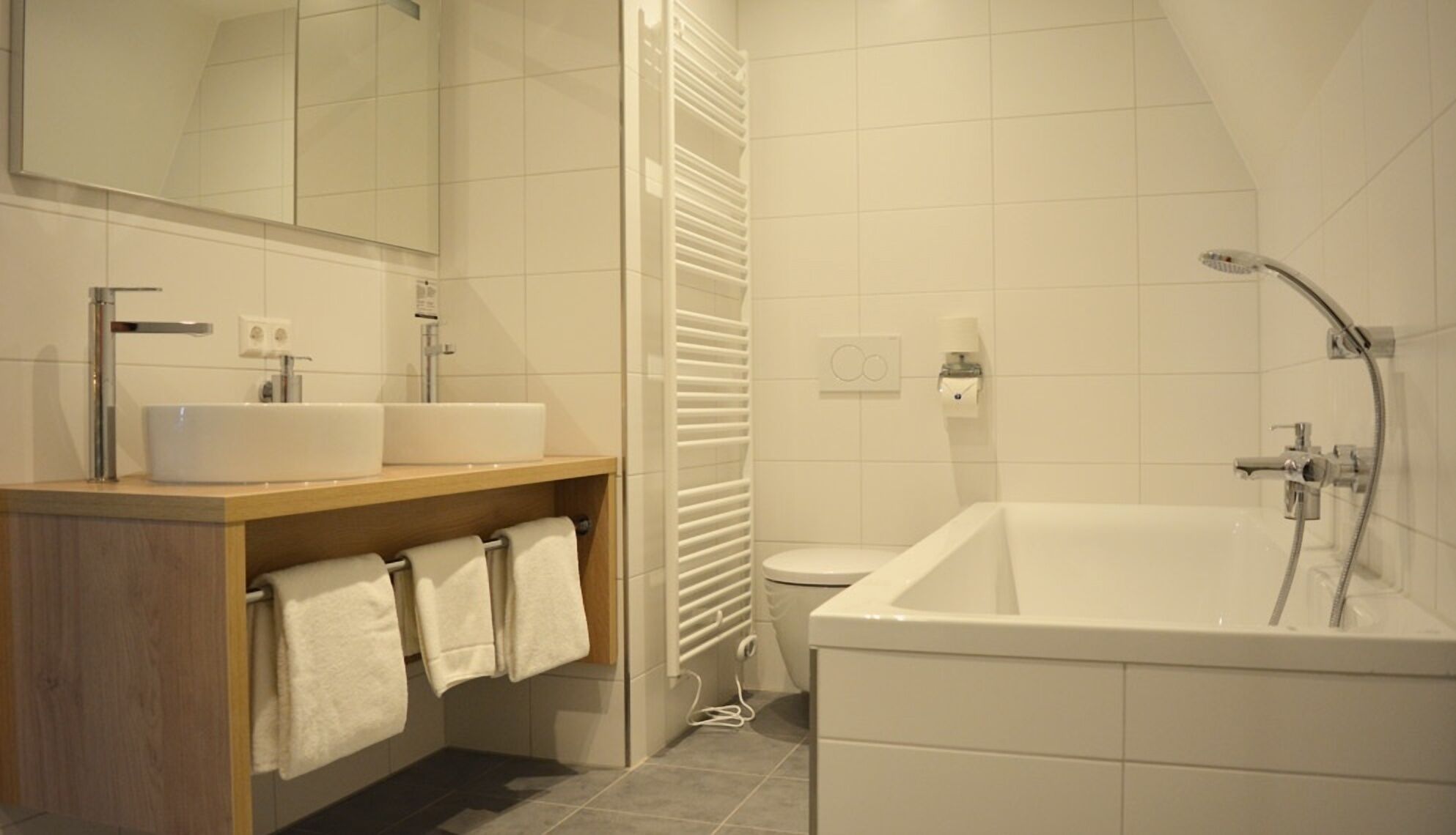 Een moderne badkamer met een ruim bad, een houten wastafelmeubel met twee wastafels en een handdoekrek.