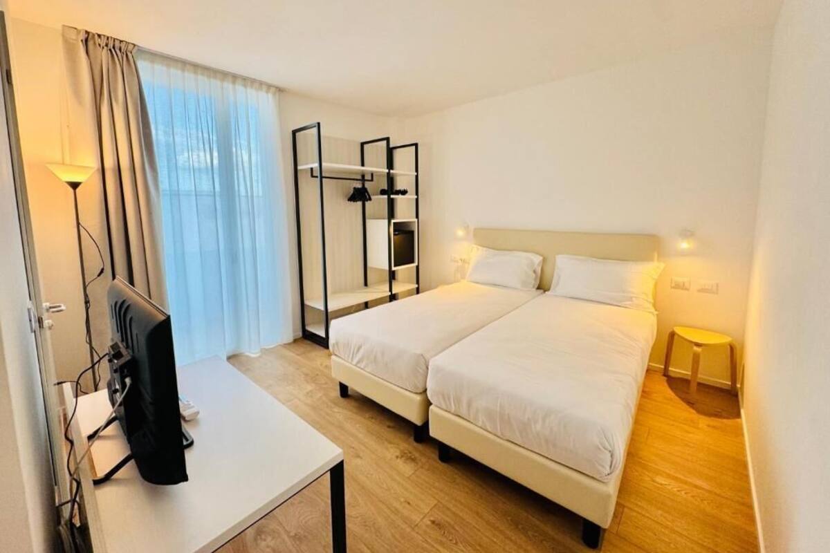 Habitación de hotel con dos camas, televisión, escritorio y ventana con cortinas.