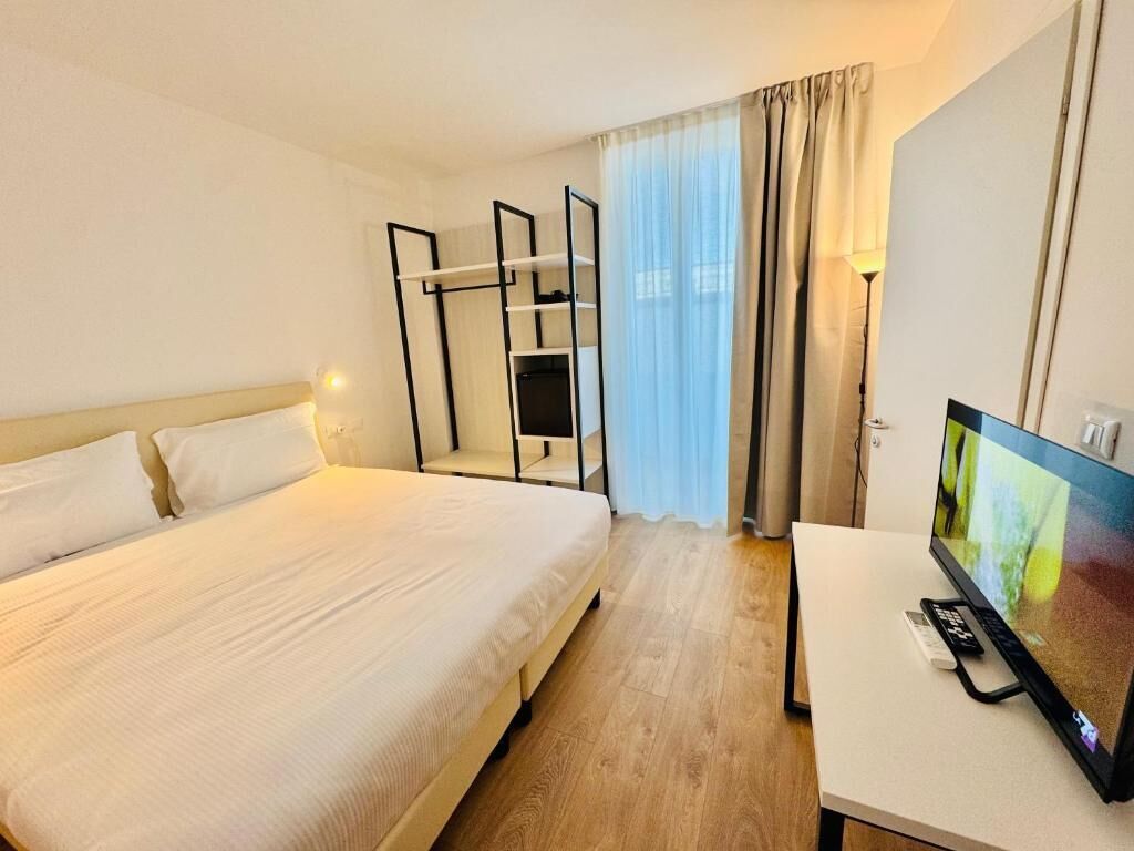 Hotellihuone, jossa on sänky, työpöytä, jossa on televisio, ja ikkuna, jossa on verhot.