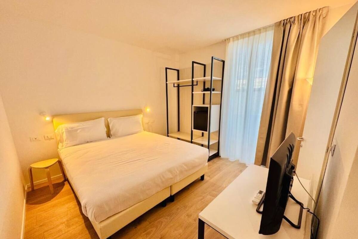 Habitación de hotel con cama, mesita de noche, televisor y un taburete pequeño.