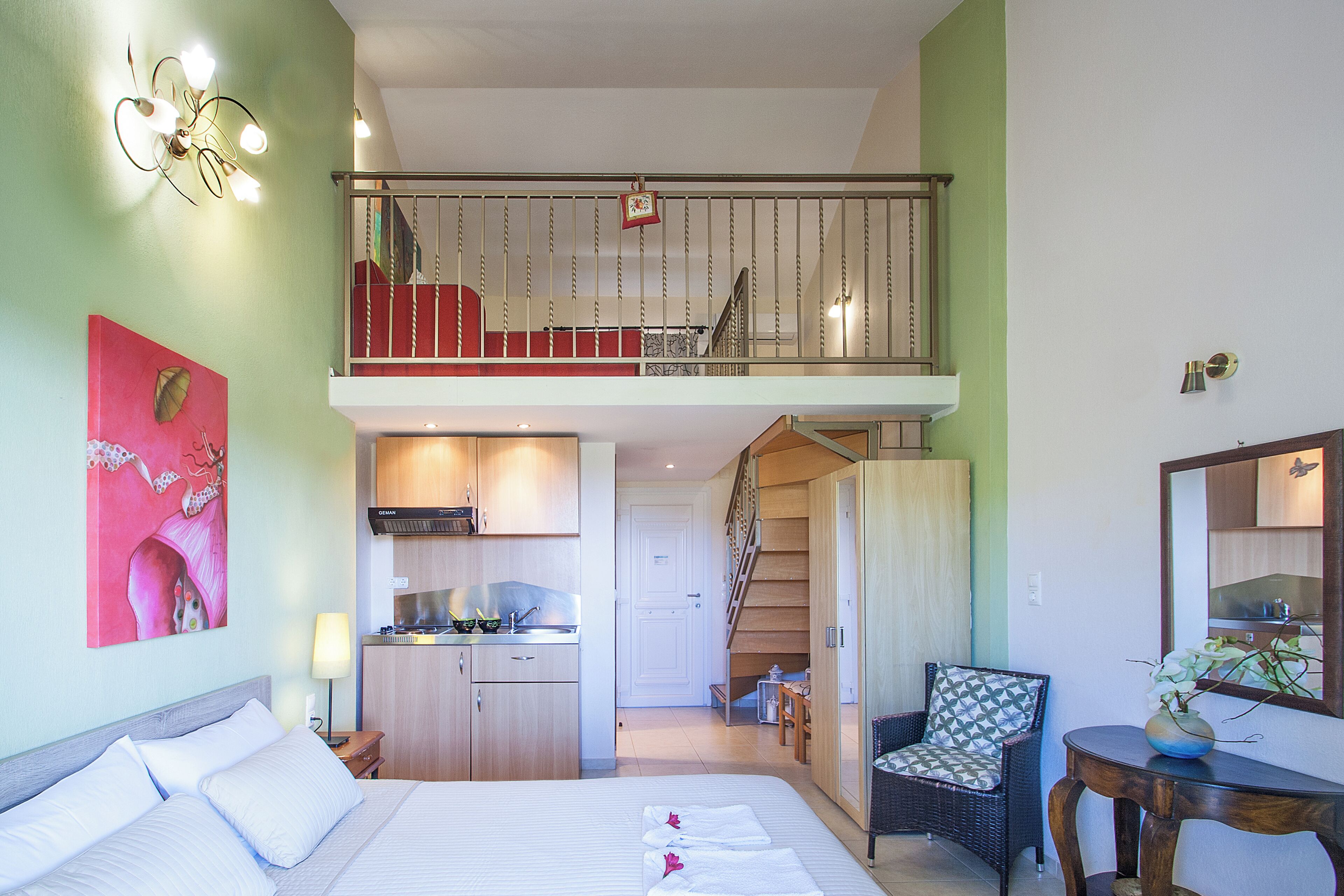 Een hotelkamer met een bed, een eettafel, een stoel, een kitchenette en een trap naar een hoger niveau.