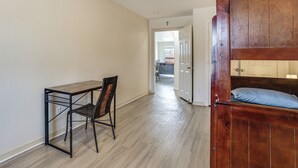 Ein Schlafzimmer mit einem Holzbett, einem Schreibtisch mit Stuhl und einer Tür zu einem weiteren Raum.