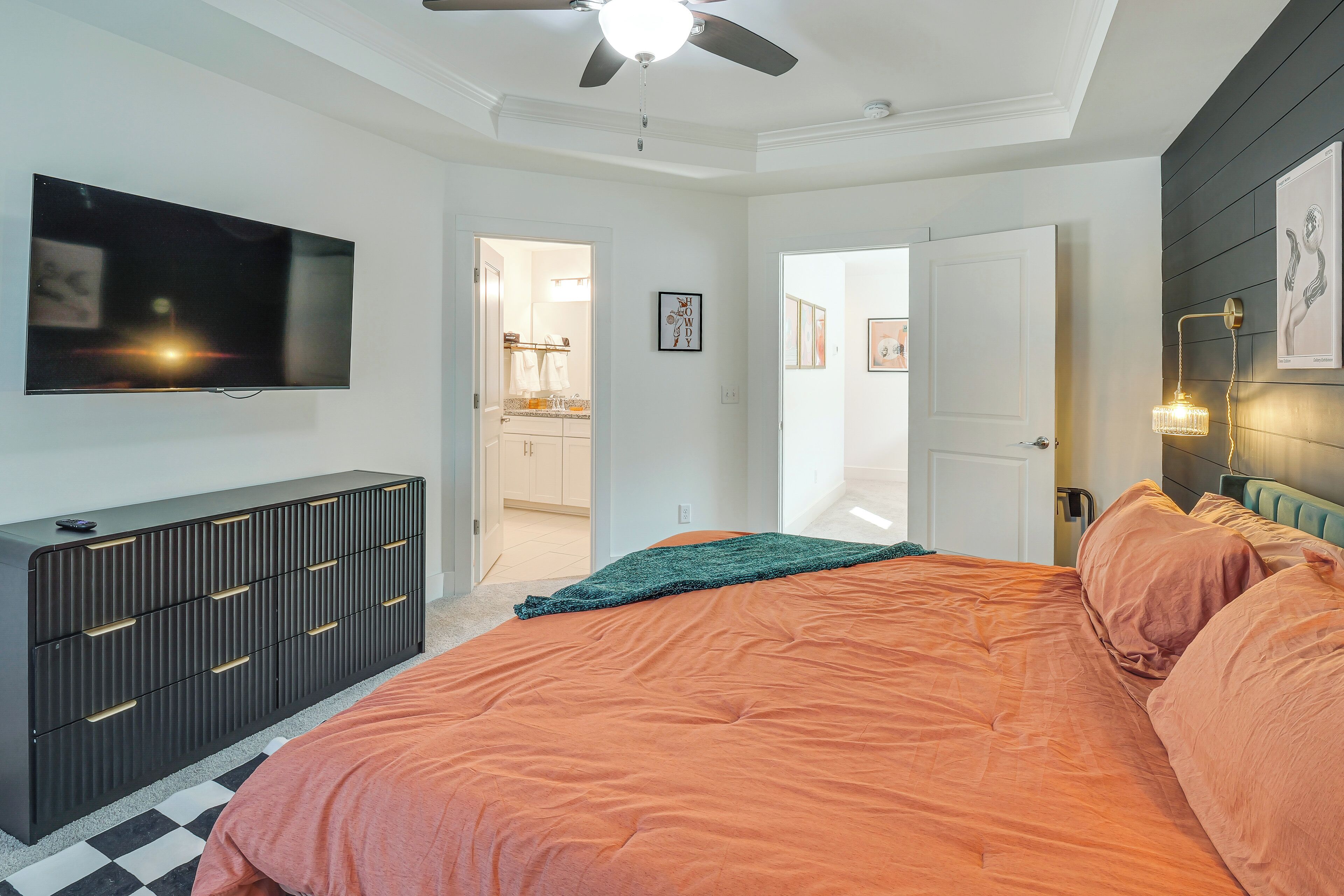 A bedroom with a large bed, a dresser, a TV mounted on the wall, and a ceiling fan.
