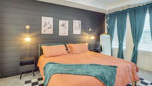 Ein Schlafzimmer mit einem Bett, zwei Nachttischen, einem kleinen Tisch, einem karierten Teppich und einem Fenster mit Vorhängen.