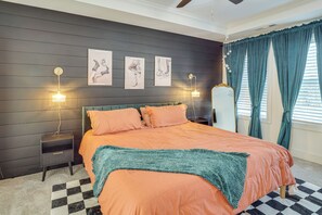 Ein Schlafzimmer mit einem Bett, zwei Nachttischen, einem kleinen Tisch, einem karierten Teppich und einem Fenster mit Vorhängen.