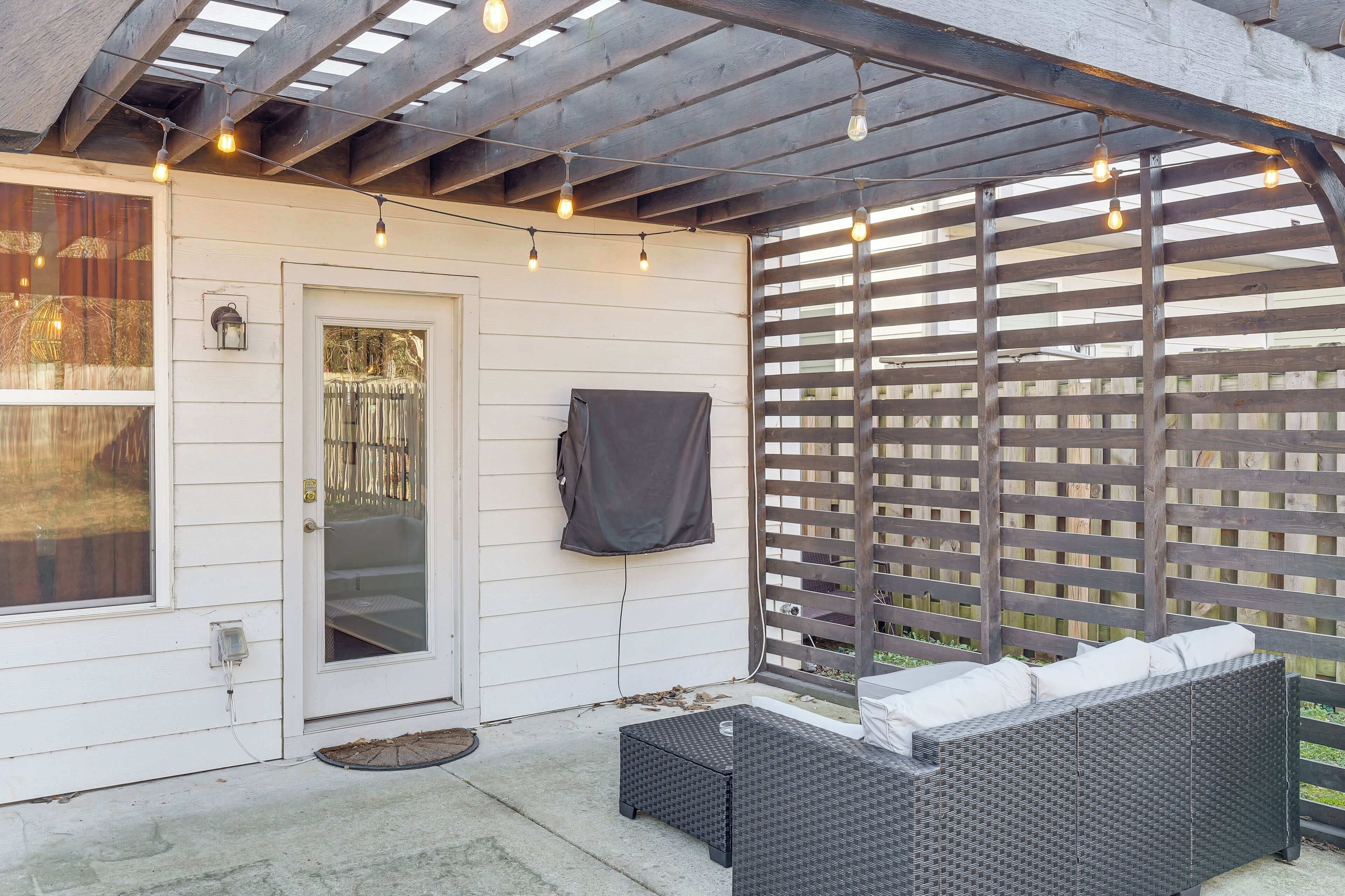 A covered patio with a wicker sofa, string lights, and a wooden fence.
