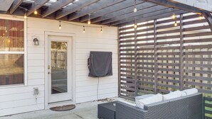 Eine überdachte Terrasse mit einem Rattangeflechtsessel, Lichterketten und einem Holzzaun.