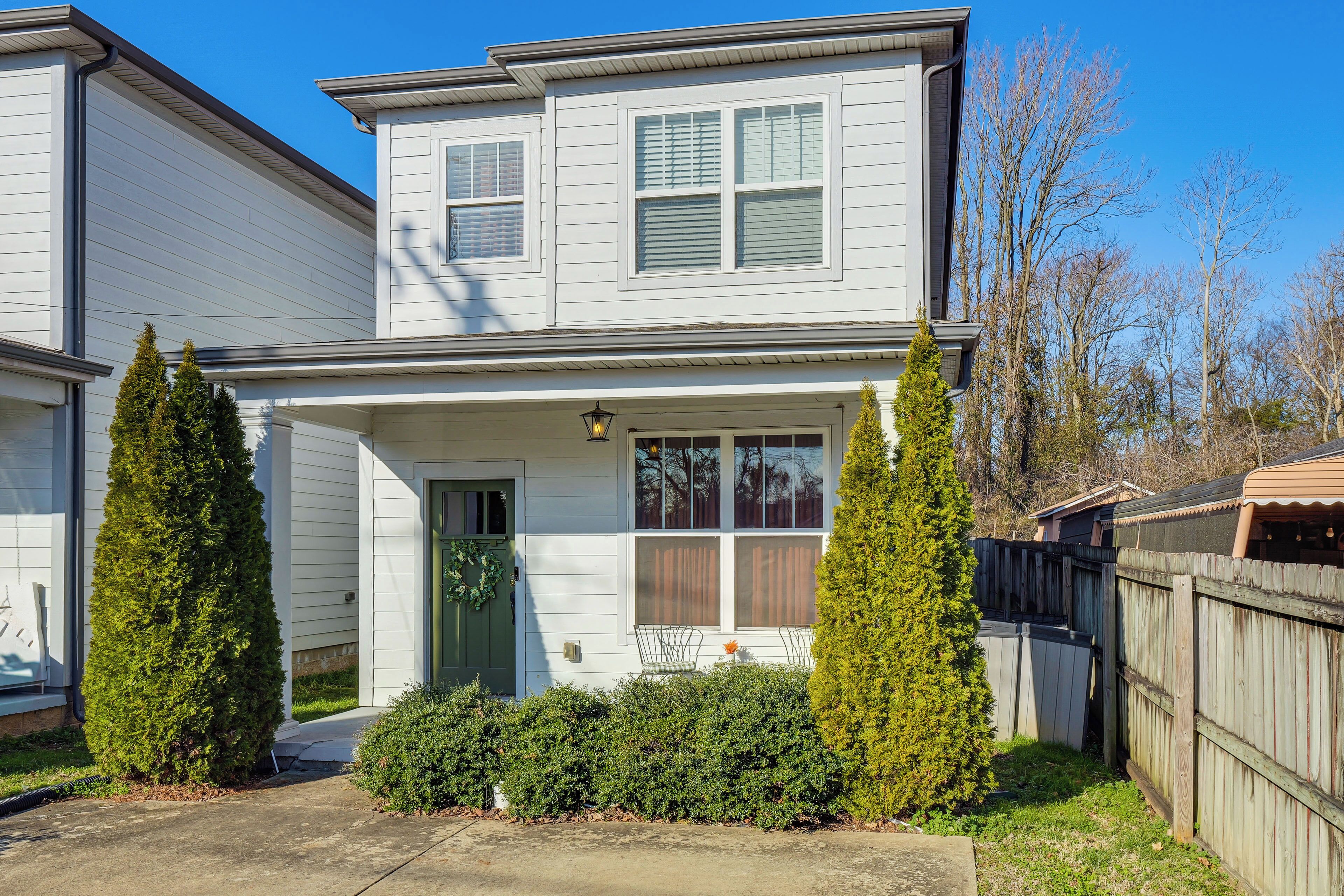 A two-story house with a front porch, a green door, and a wooden fence.