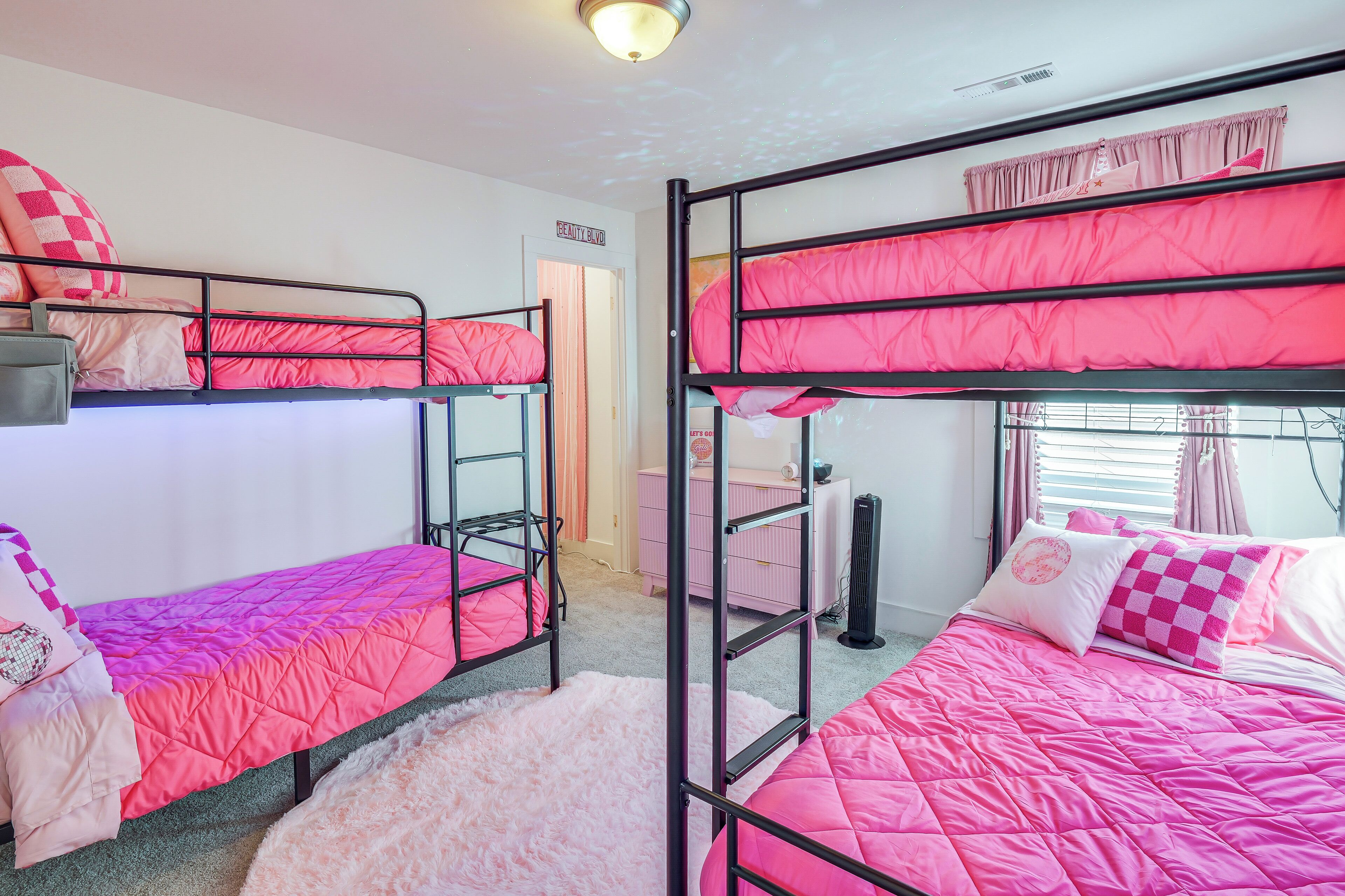 A bunk bed room with pink bedding, a fluffy rug, and a window with curtains.