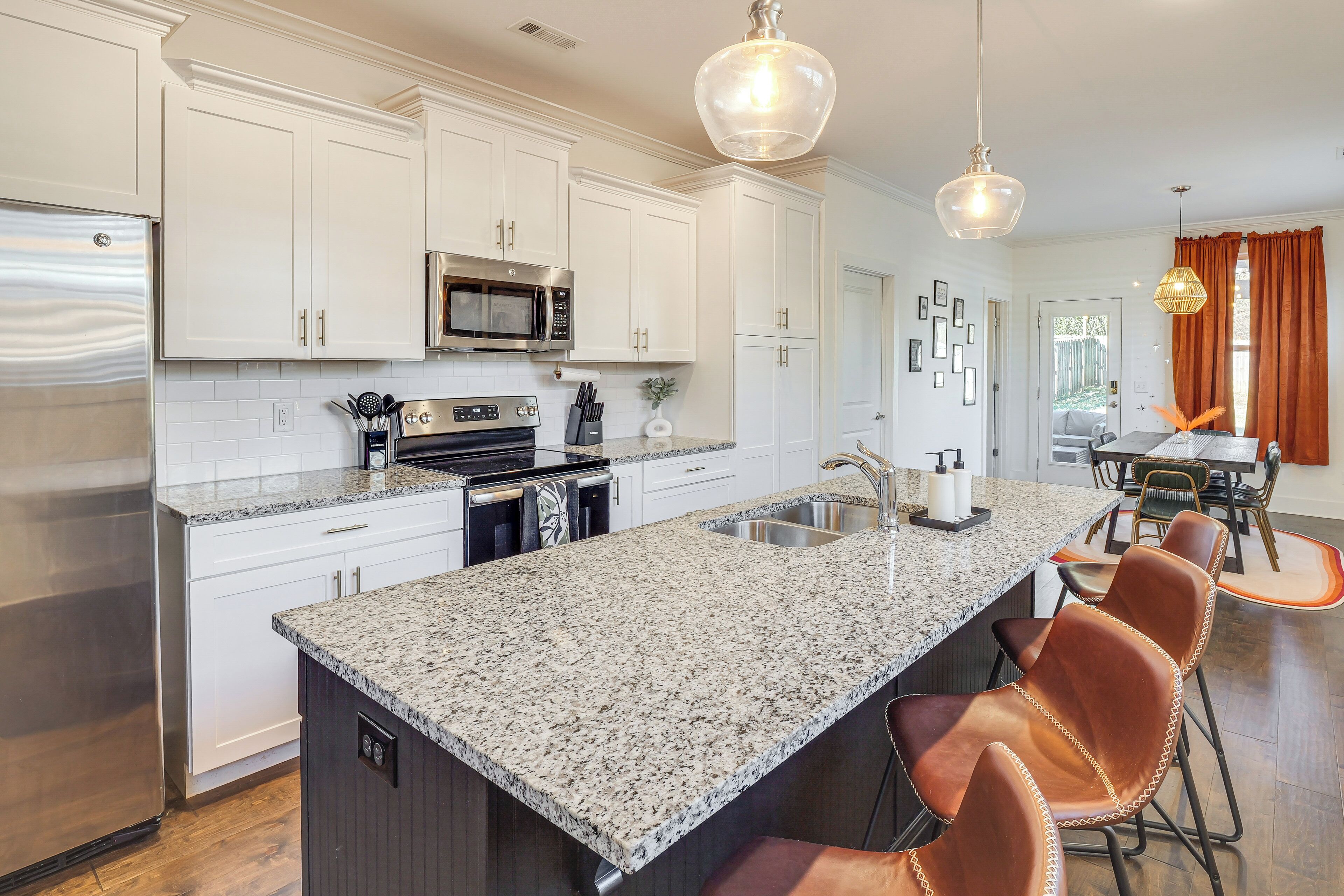 A modern kitchen with white cabinetry, stainless steel appliances, granite countertops, and a central island with bar stools.