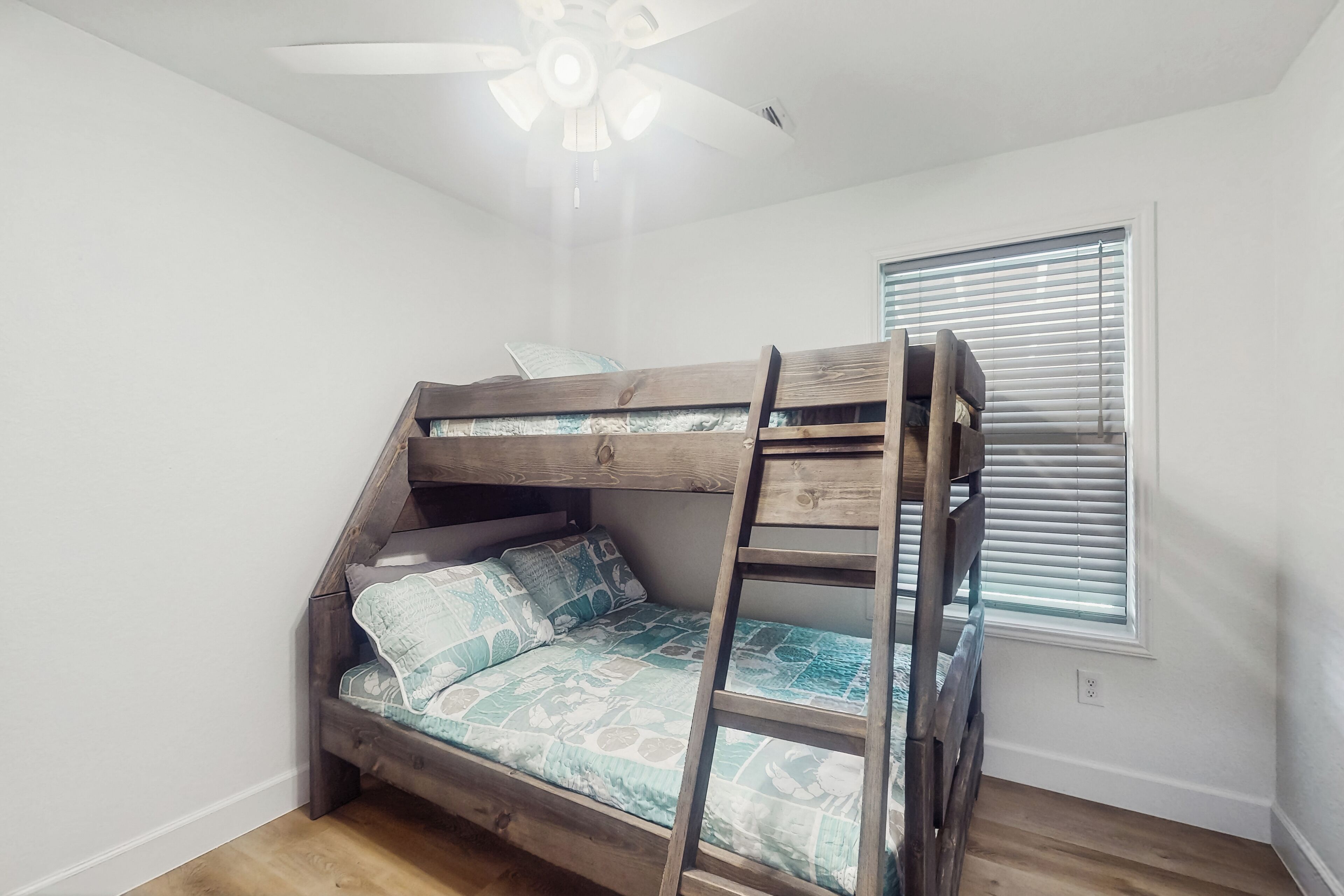 Een stapelbed met een ladder, een plafondventilator en een raam met zonwering.