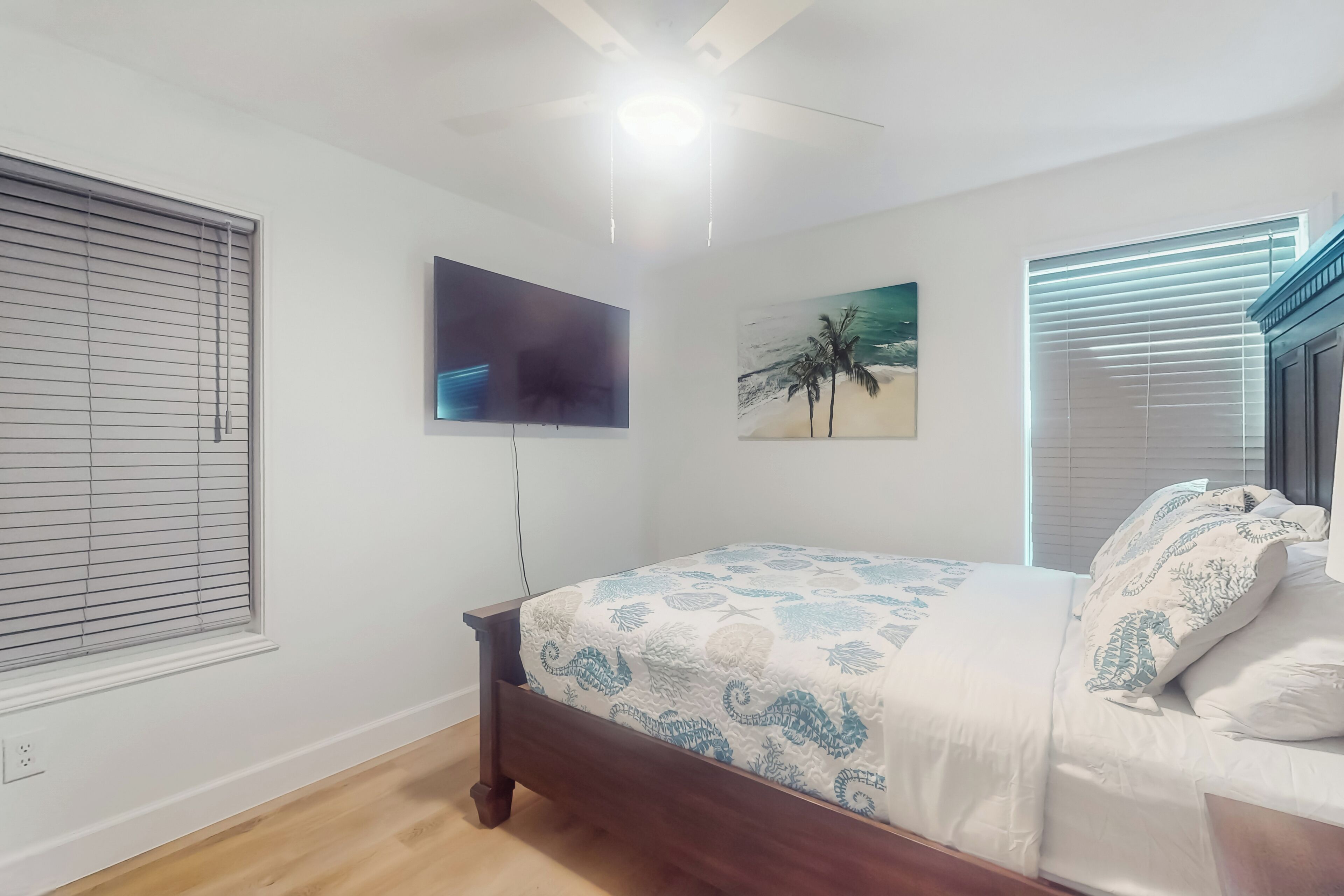 Un dormitorio con cama, ventilador de techo, televisión y un cuadro en la pared.