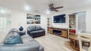A modern living room with a sofa, TV, fireplace, and decorative shelves. - 3BR Coastal Home w/ Coastal Design- Steps to Sand (Galveston)