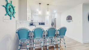A modern kitchen with white cabinets, a central island, and a blue and white chair arrangement. - 3BR Coastal Home w/ Coastal Design- Steps to Sand (Galveston)