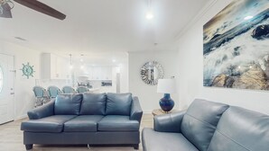 A modern living room with a dark leather sofa, a round mirror, and a painting of a mountainous landscape. - 3BR Coastal Home w/ Coastal Design- Steps to Sand (Galveston)