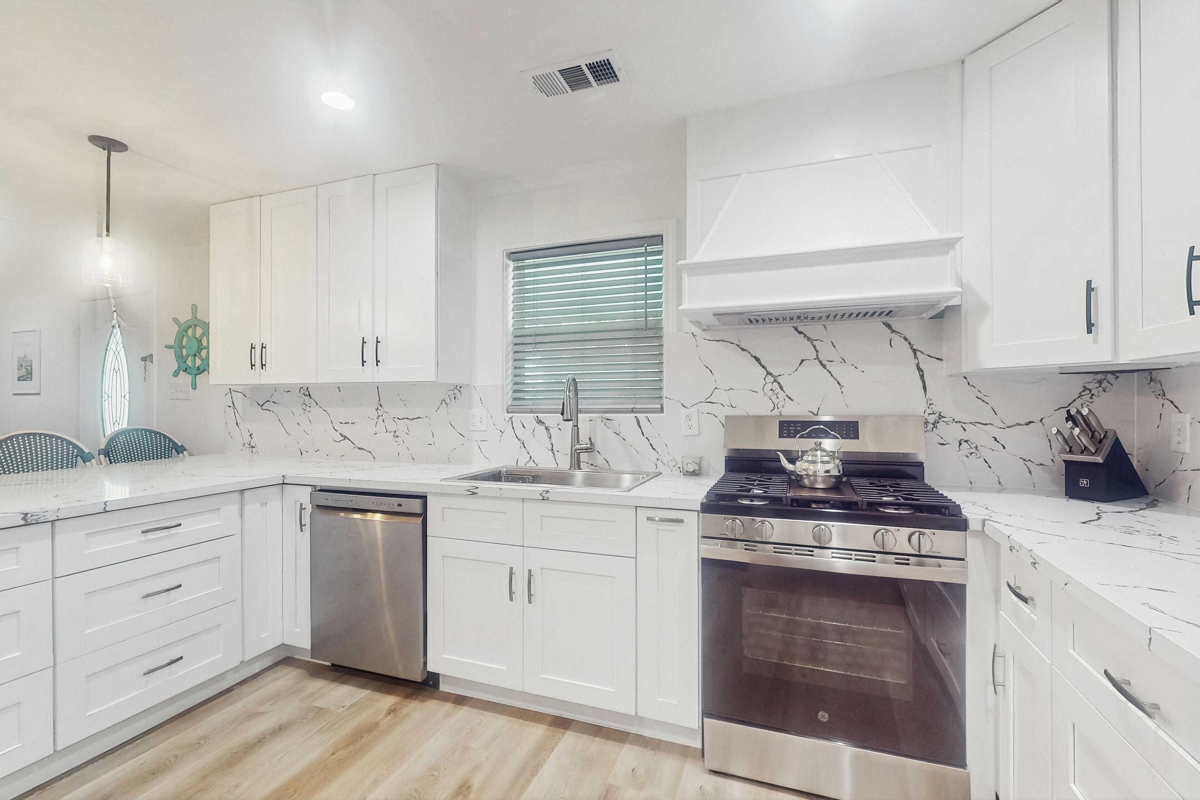 A modern kitchen with white cabinets, a stainless steel dishwasher, a gas stove, and a built-in oven.