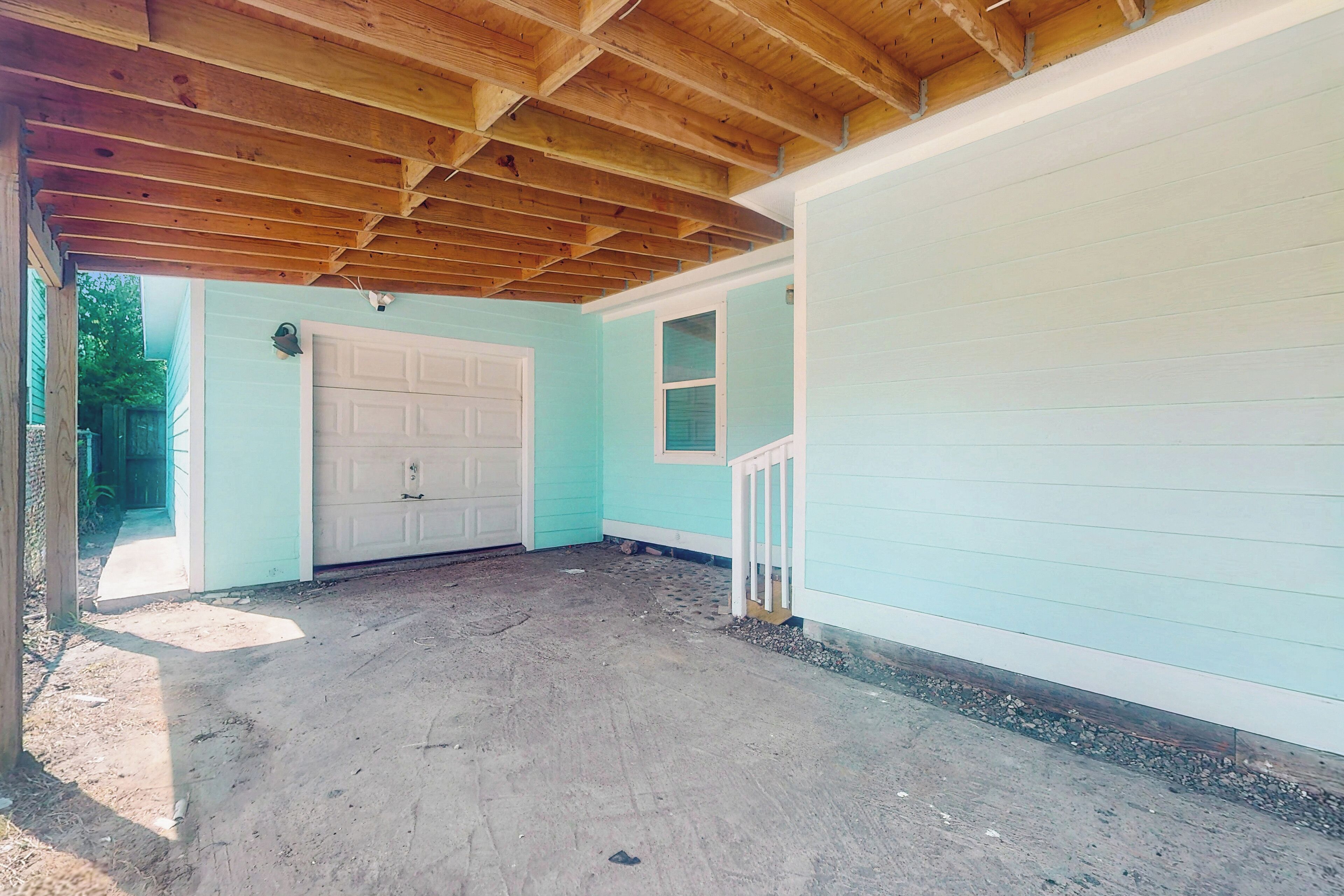 Un portico coperto con soffitto in legno, un portone garage bianco e una parete esterna azzurra.