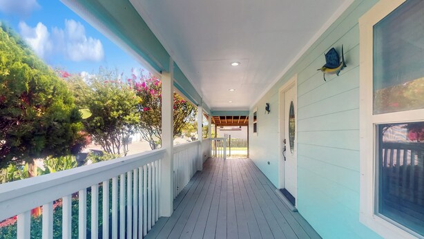 A covered porch with a wooden floor and white railings, leading to a covered entrance. - 3BR Coastal Home w/ Coastal Design- Steps to Sand (Galveston)