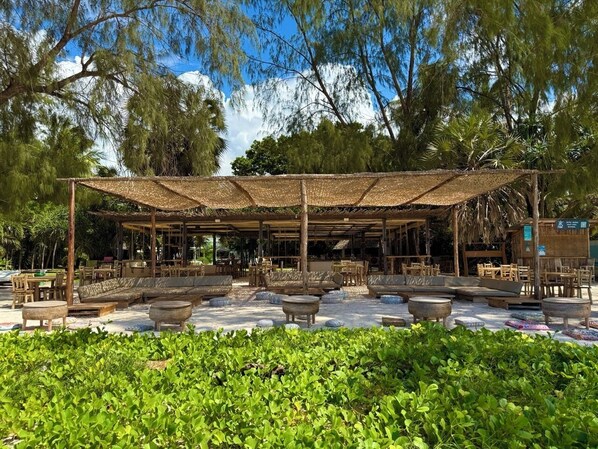 An outdoor seating area with wooden furniture and a thatched roof structure. - Galu Ecolodge (Diani Beach)