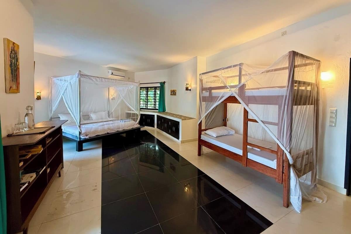 A room with two beds, a bench, a small table, and a wall-mounted air conditioner.