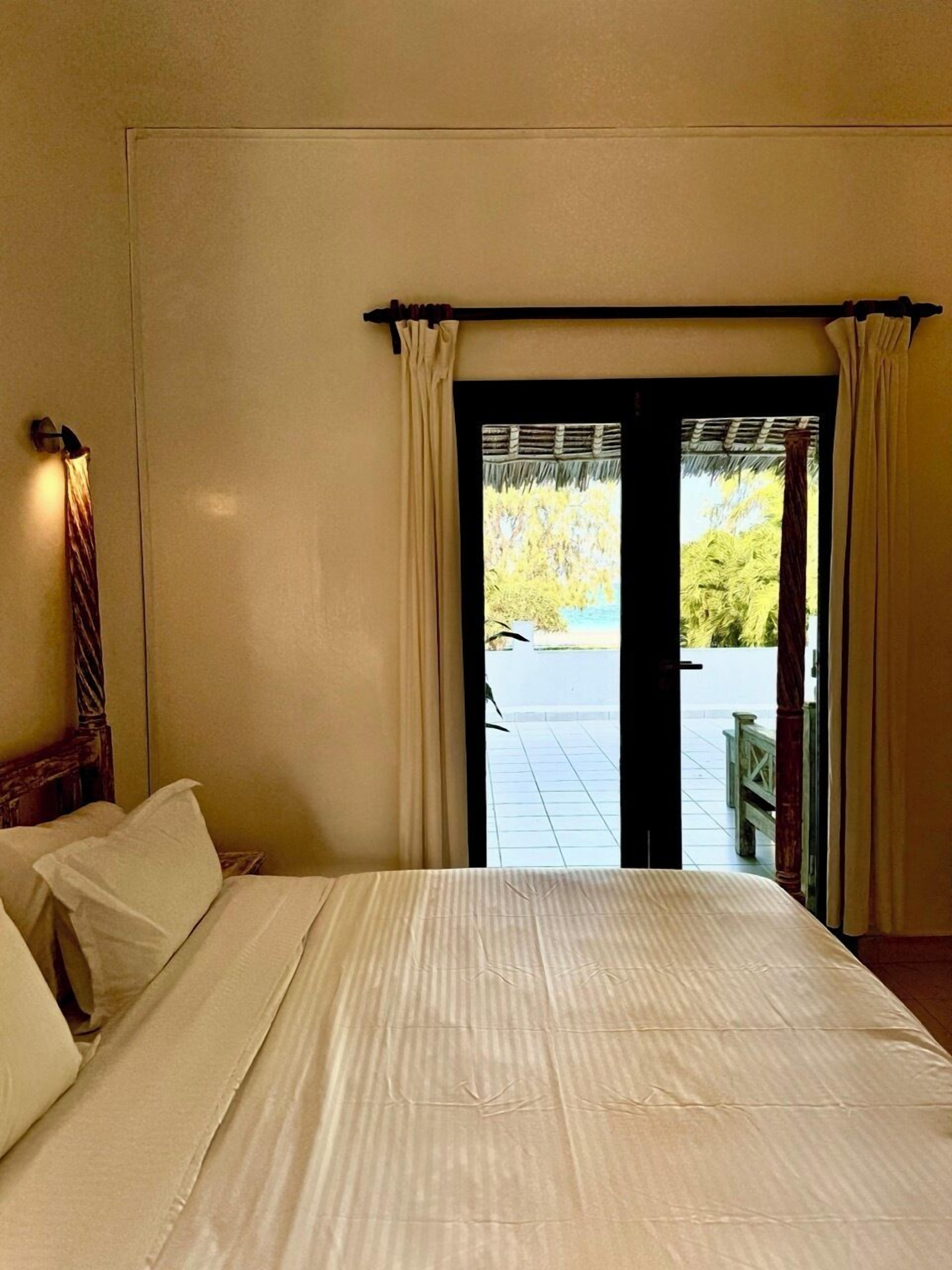 A hotel room with a bed, curtains, and a view of the outdoors.