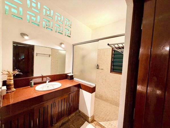 A bathroom with a sink, mirror, and shower area.