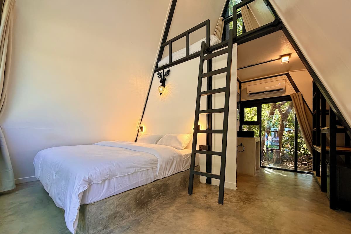 A bedroom with a bunk bed, a ladder, a bedside table, and a window with a view of trees.