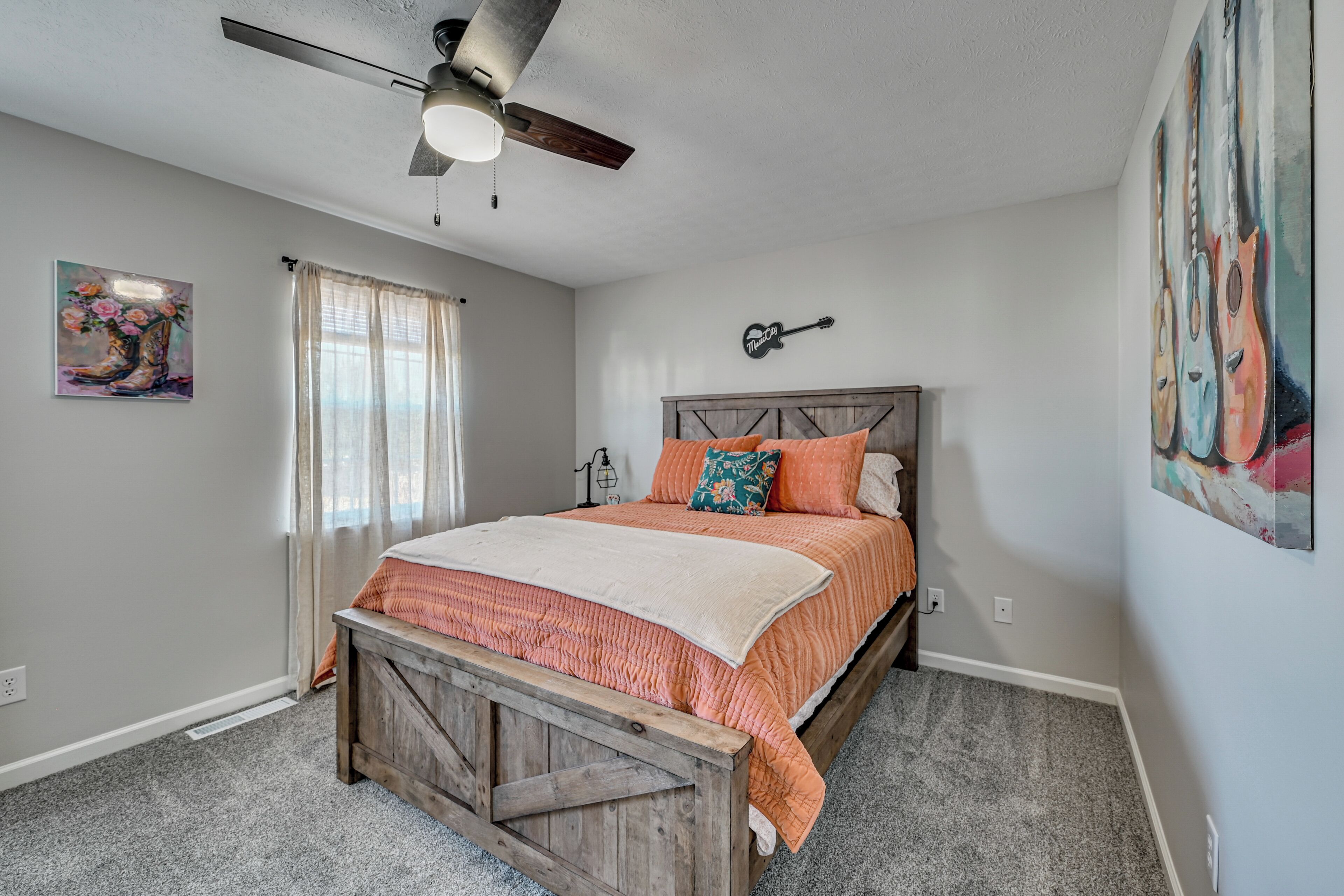 A bedroom with a bed, a ceiling fan, a window with curtains, and a wall-mounted guitar decoration.