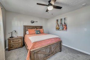 Une chambre à coucher comprenant un lit, une table de chevet, un ventilateur de plafond, une décoration murale représentant une guitare et un tableau de guitares.