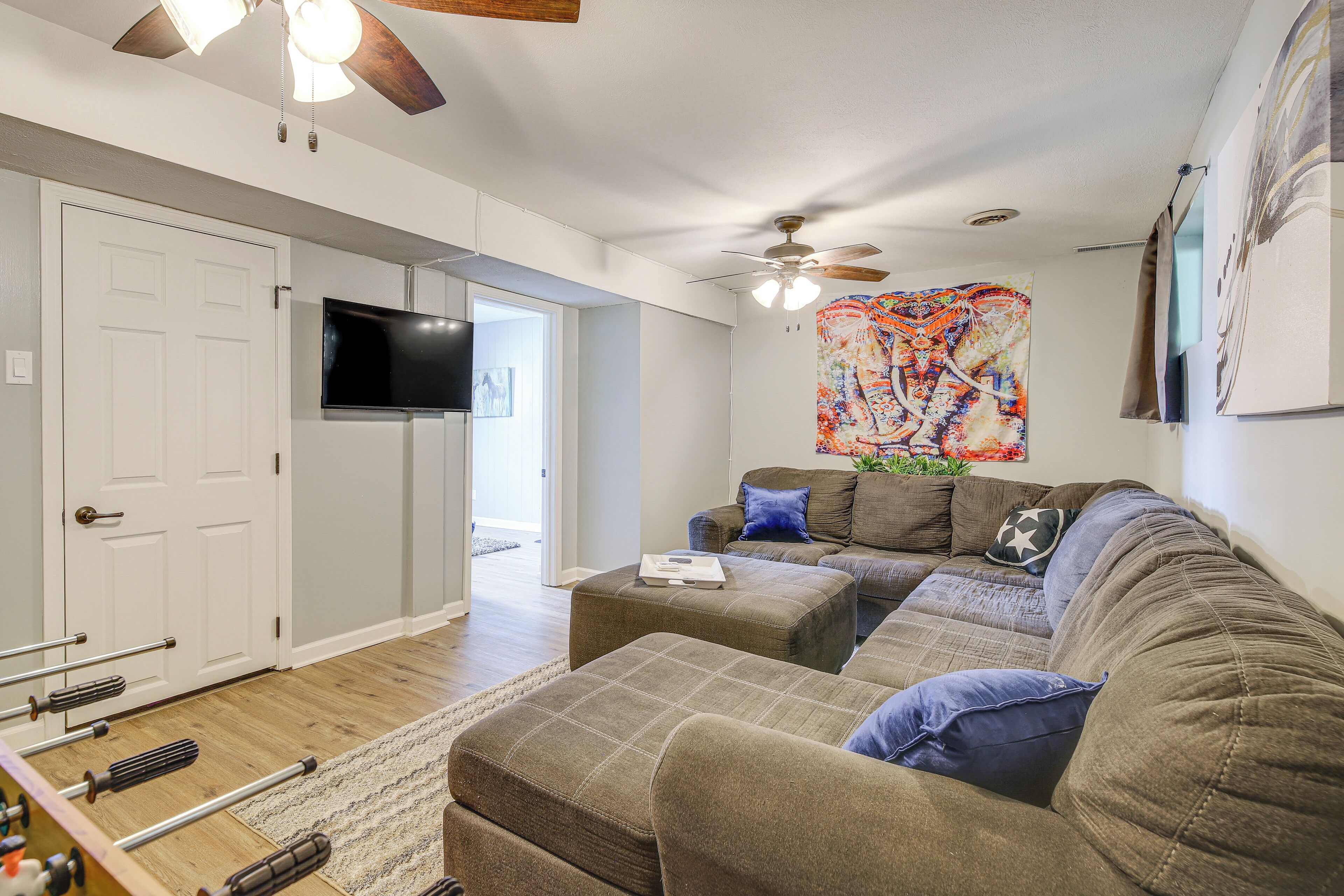 A living room with a sectional sofa, ottoman, and a flat-screen TV mounted on the wall.