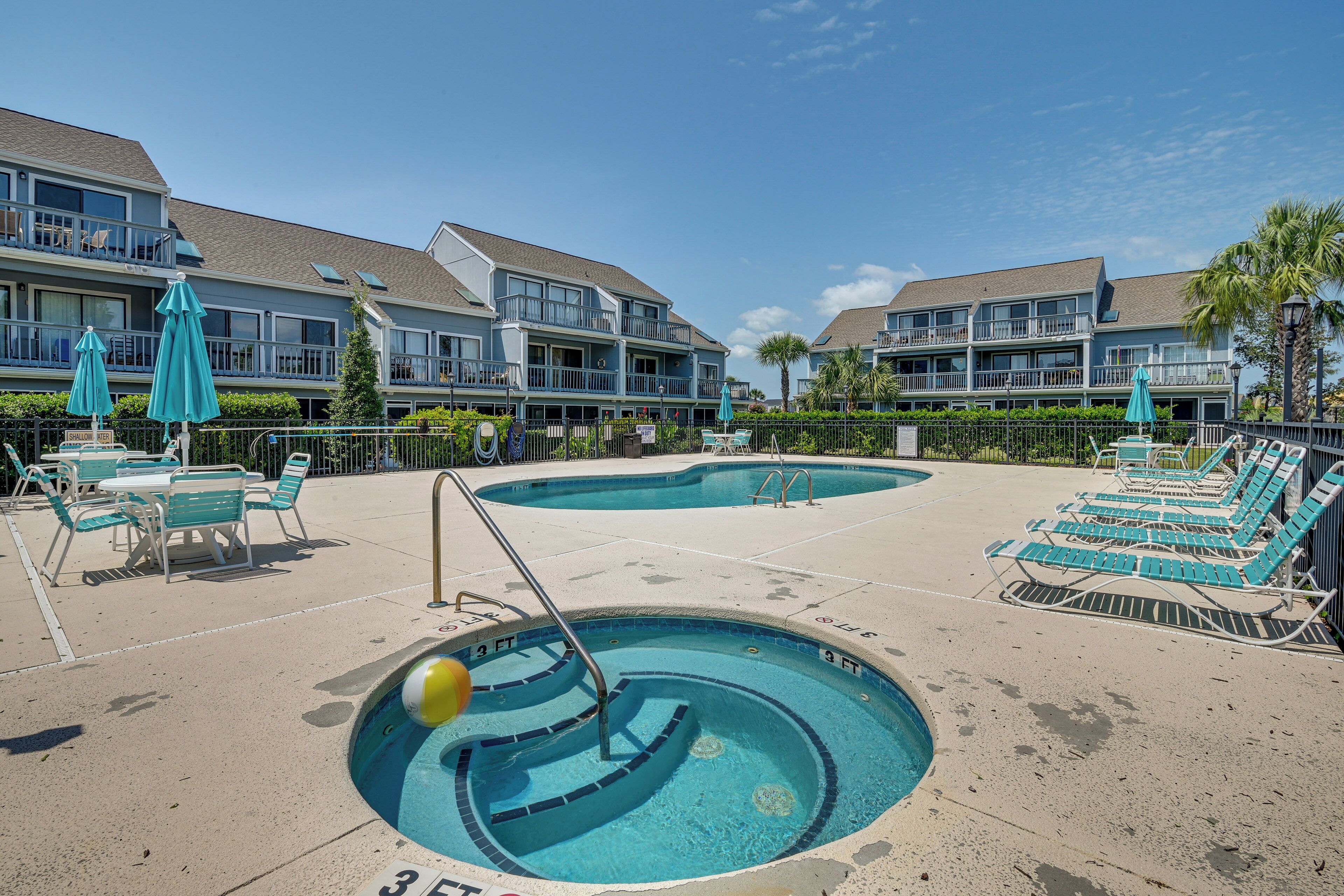 A pool area with lounge chairs and umbrellas, surrounded by a building with balconies.