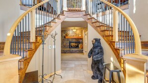 A grand staircase with a bear statue at the bottom, leading to a stone fireplace and a second floor. - Ski-in/ski-out! Mtn-view Donnelly Home w/ Hot Tub (Donnelly)