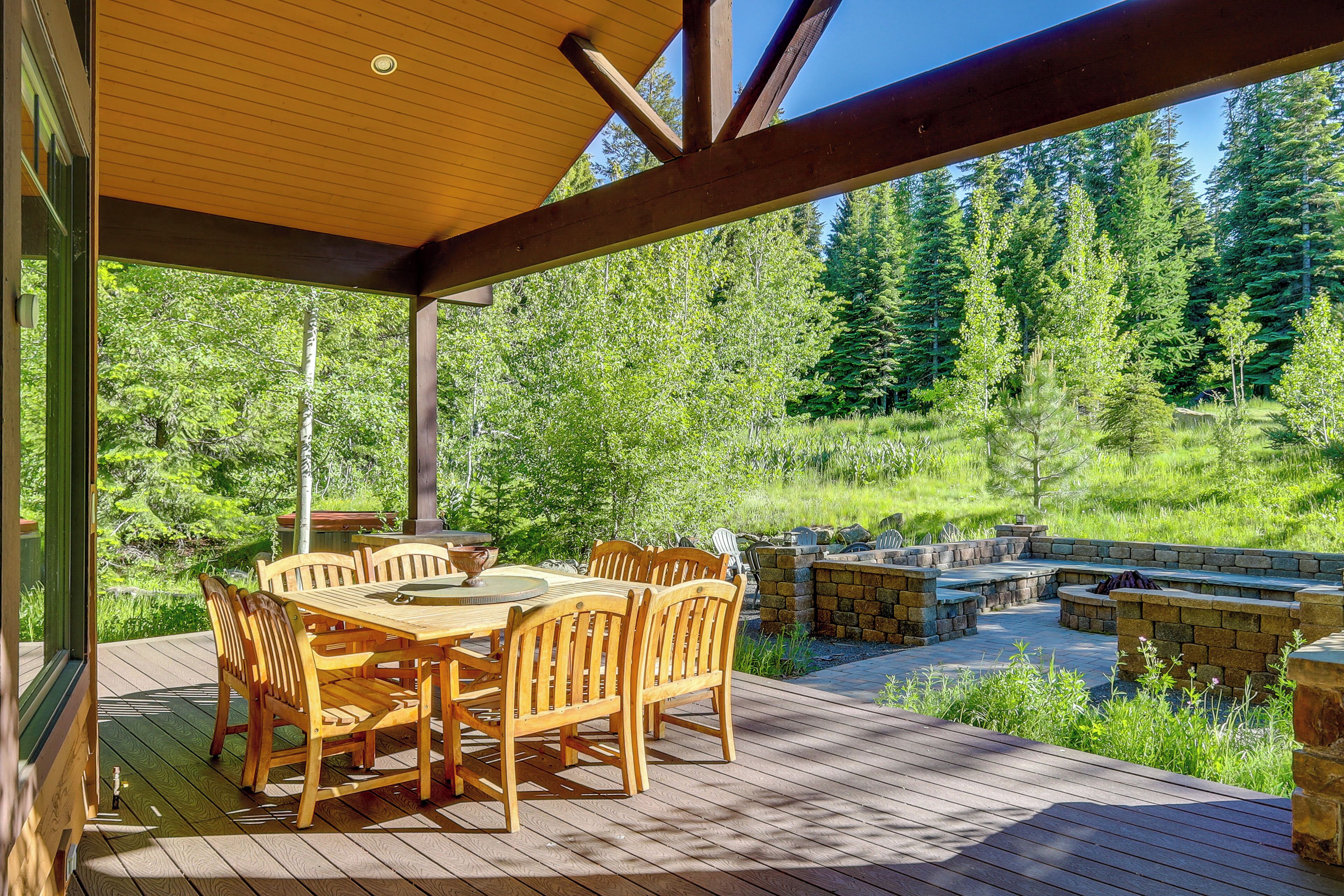 A wooden deck with a round table and chairs, stone seating, and a view of a forest.