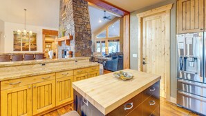 A spacious kitchen with wooden cabinets, a stone accent wall, a large island, and a stainless steel refrigerator. - Ski-in/ski-out! Mtn-view Donnelly Home w/ Hot Tub (Donnelly)