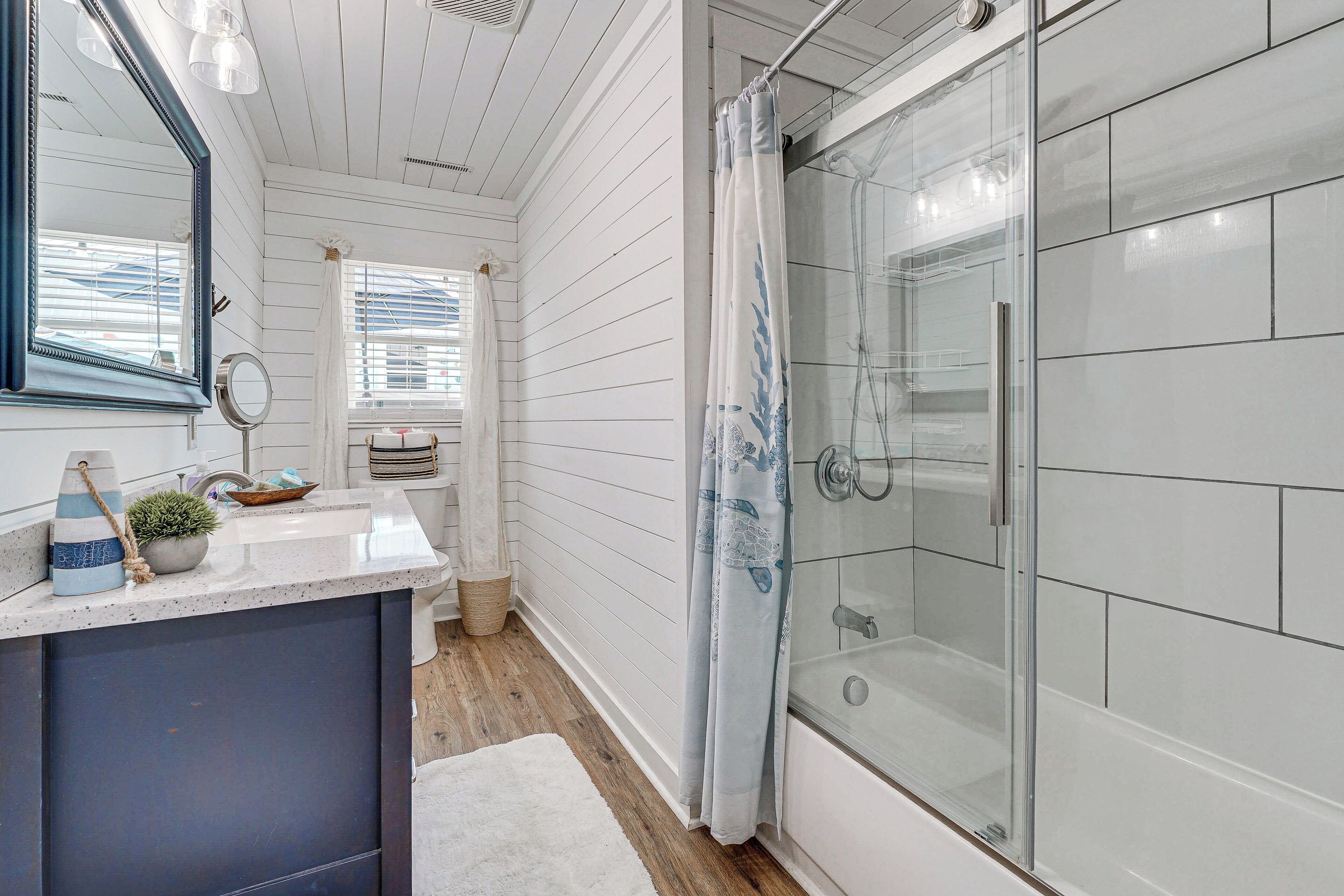 A bathroom with a white vanity, a glass shower enclosure, and a window with blinds.