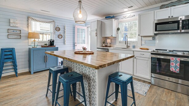 A kitchen with a wooden island, blue bar stools, white cabinets, and a stainless steel oven. - < 1 Mi to Beach: Oak Island Retreat w/ Swim Spa! (Oak Island)