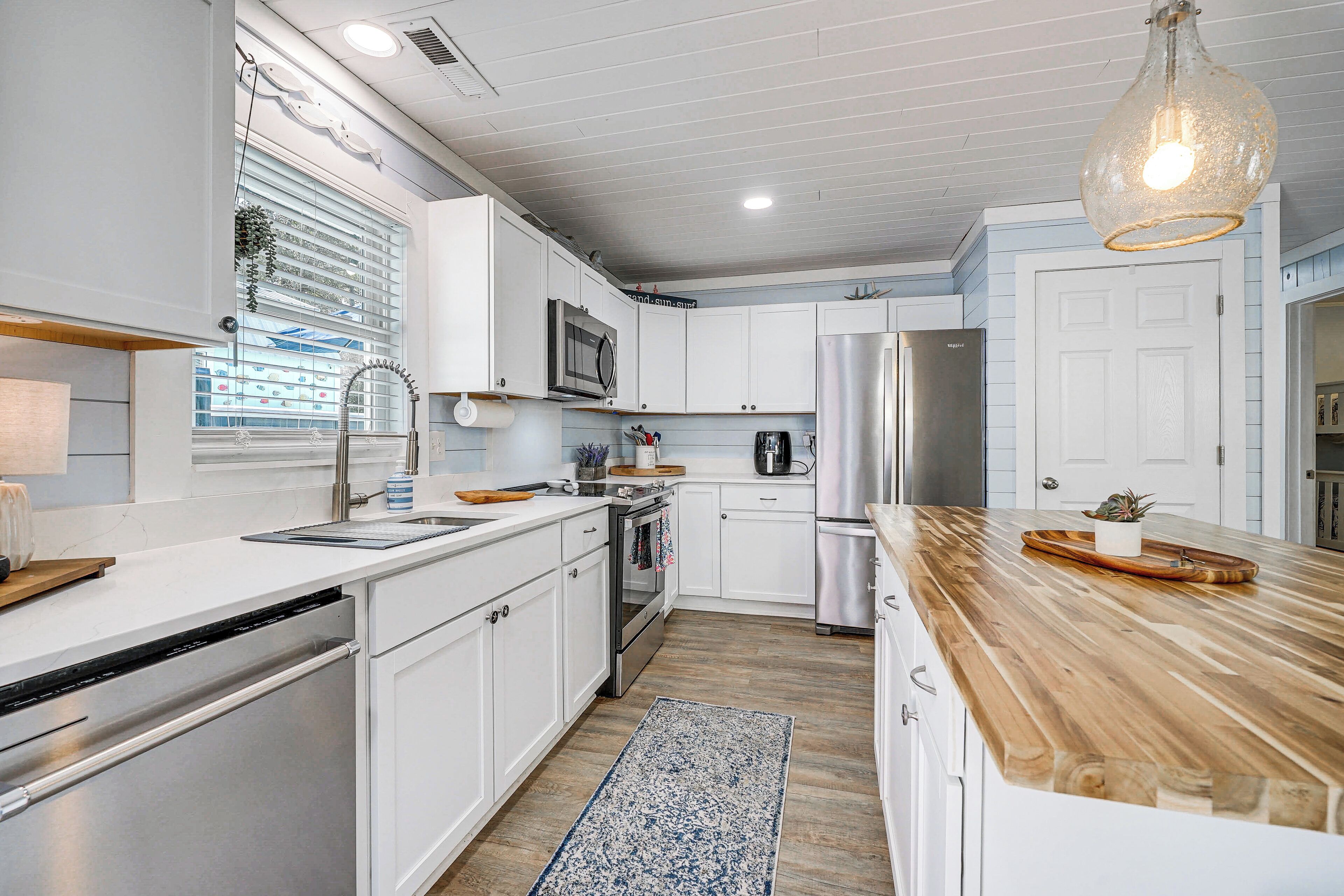 A modern kitchen with white cabinets, stainless steel appliances, a wooden countertop, and a hanging light fixture.