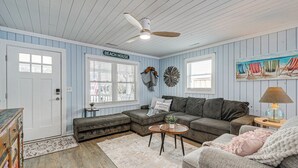 A beach-themed living room with a sectional sofa, a round coffee table, and a ceiling fan. - < 1 Mi to Beach: Oak Island Retreat w/ Swim Spa! (Oak Island)