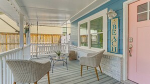 A covered porch with wicker chairs, a small table, and a potted plant. - < 1 Mi to Beach: Oak Island Retreat w/ Swim Spa! (Oak Island)