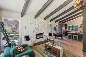 A spacious living room with a fireplace, a green sofa, a dining area, and a kitchen with a large island. - Modern Forest Escape, Near Lake Stevens & Hikes (Lake Stevens)