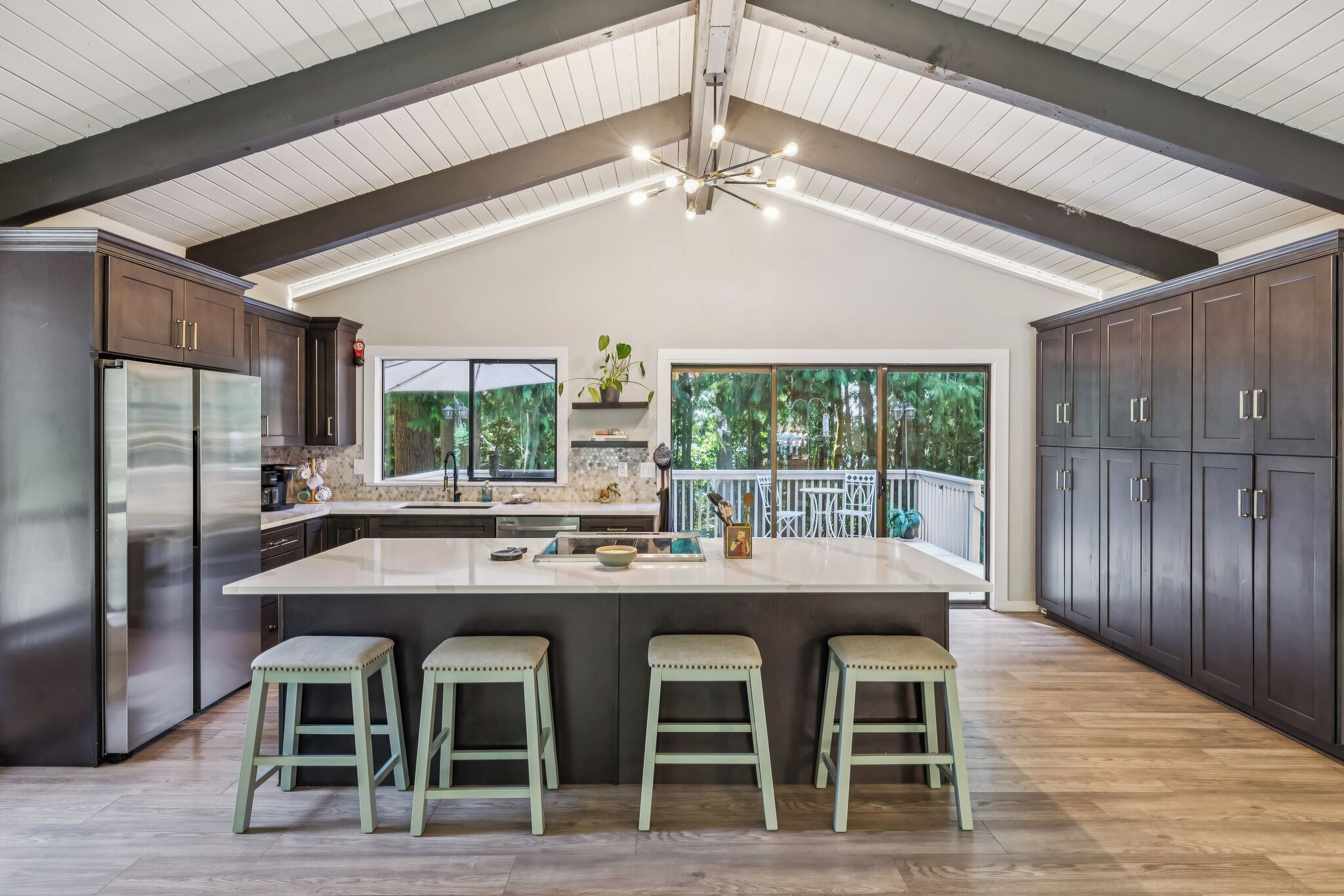 A modern kitchen with a large island, dark cabinetry, and a high ceiling with exposed beams.
