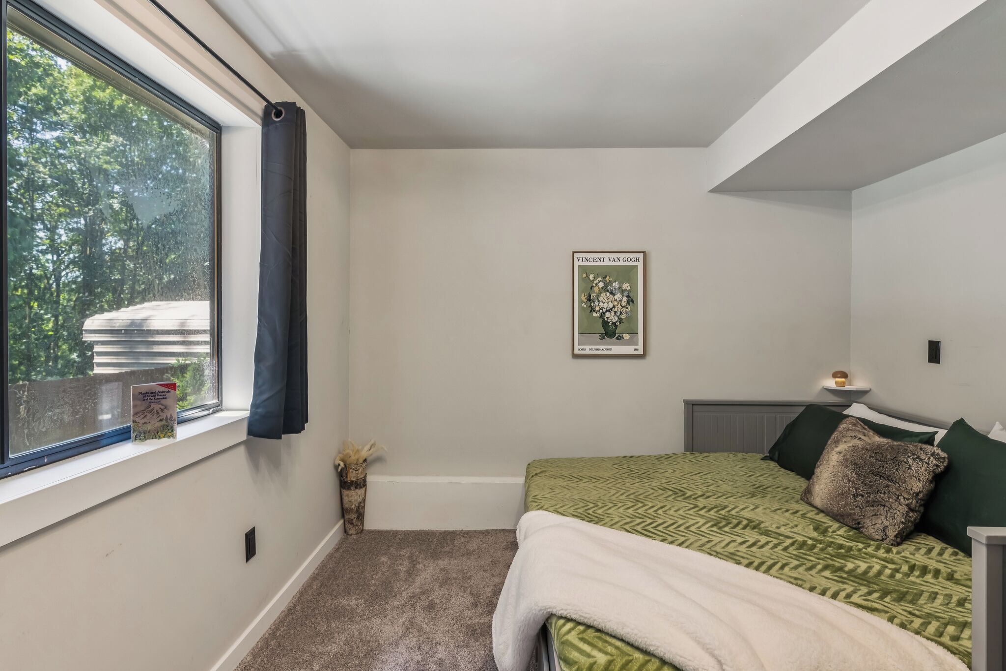 Un dormitorio con cama, ventana, un cuadro enmarcado y una mesita de noche.