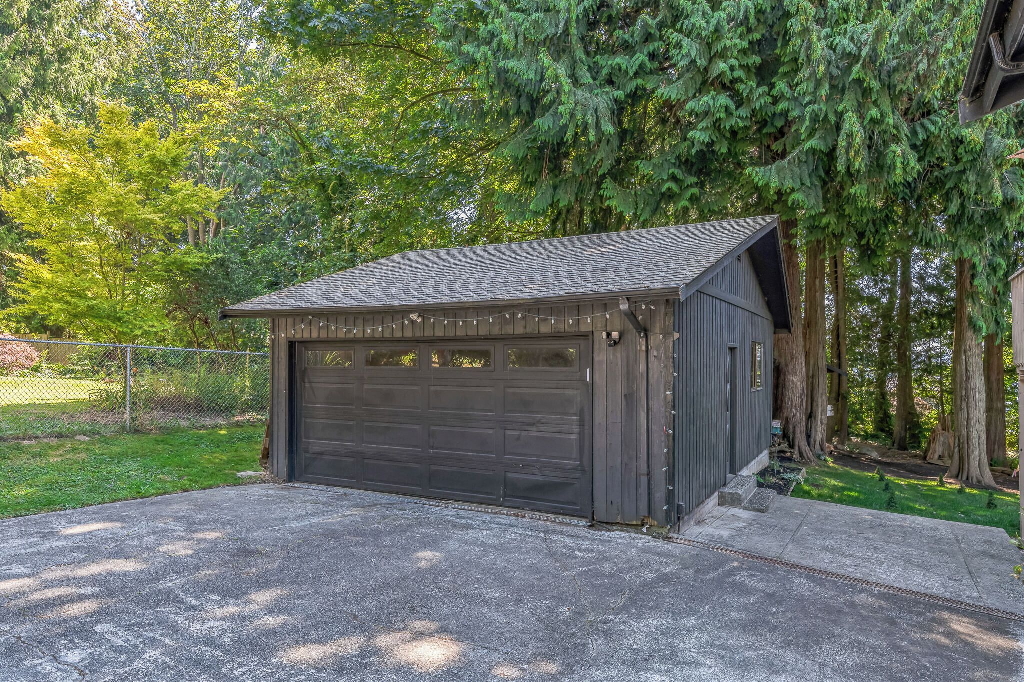 Eine kleine, dunkel gefärbte Garage mit geneigtem Dach, umgeben von einem Rasen und hohen Bäumen.