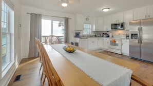 Une cuisine moderne avec des meubles blancs, des appareils en acier inoxydable et une table à manger en bois sur laquelle se trouve un saladier rempli de fruits.