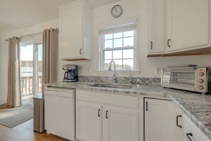 A kitchen with white cabinets, a sink, a coffee maker, a toaster, and a clock on the wall. - Waterfront Gem w/ Deck & Views on Chesapeake Bay! (Reedville)