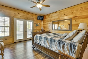 A wooden-paneled bedroom with a bed, a ceiling fan, a TV, and a large mirror. - Steps to Private Beach! Family Home on Lake James (Morganton)