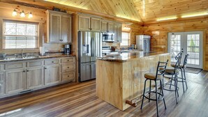 A wooden cabin-style kitchen with a central island, bar stools, and built-in appliances. - Steps to Private Beach! Family Home on Lake James (Morganton)