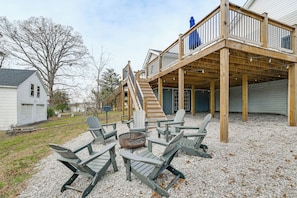 A deck with Adirondack chairs and a fire pit, wooden deck railing, and a staircase leading to a covered area.