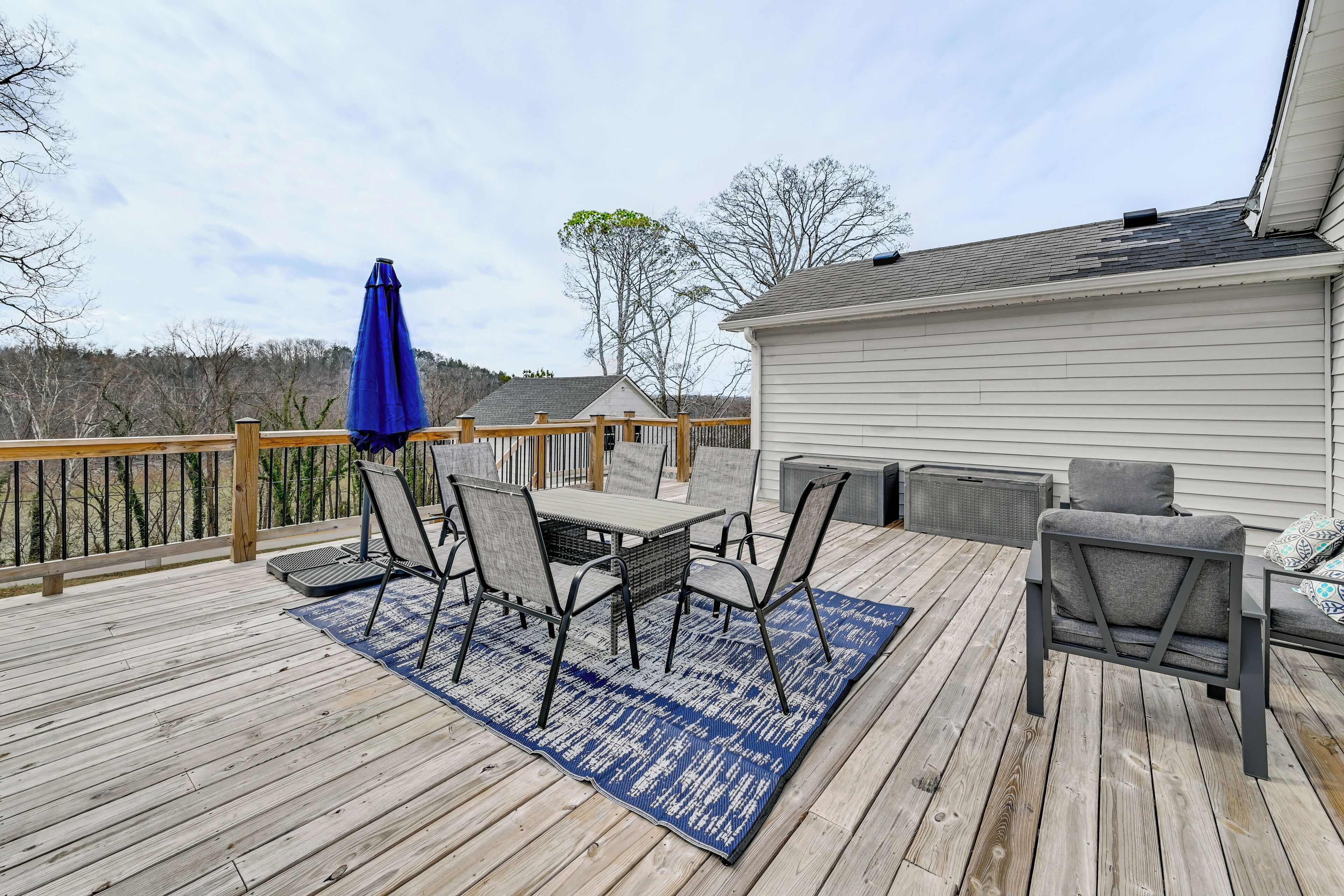 A wooden deck with a table and chairs, a blue rug, and a blue umbrella.