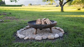 Un hogar de metal con leña en un espacio al aire libre cubierto de césped, rodeado de rocas.